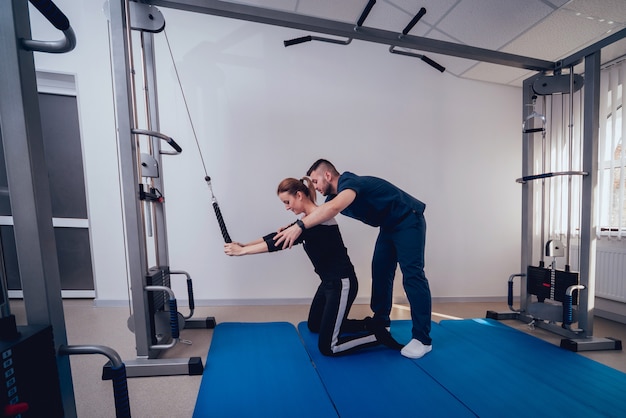 Concept of rehabilitation. Beautiful young woman doing exercises on mat under supervision of physiotherapist