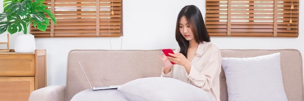 Concept of relaxation at home Young Asian woman use smartphone to chatting with friends on sofa