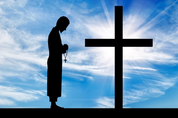 Concept of religion. Silhouette of priest and cross on a background of beautiful sky