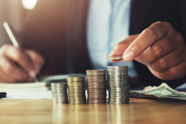 Concept saving money. hand holding coins putting stack on table in office