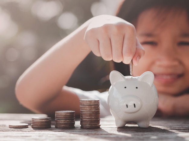 Concept of saving money. happy asian child girl save money\
putting coin into piggy bank, coins stack