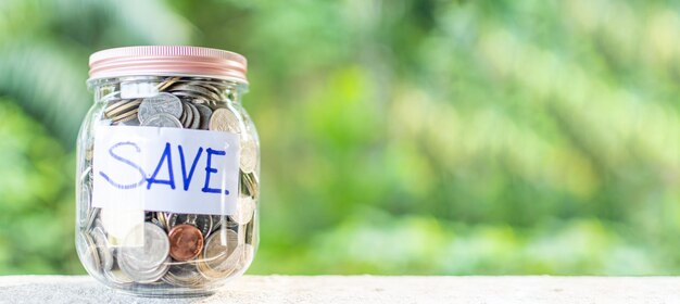 Concept of saving money for investment and emergency situations The coins and text SAVE in a glass jar placed on a wooden table Copy space top and left for content Close up Blurred background