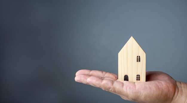Concept of selling a house A hand is holding a model house on a gray background Real estate agent