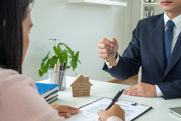 Concetto di vendita, firma e mutuo. un venditore asiatico consegna le chiavi di casa al cliente. una donna sta firmando un contratto di mutuo o compra e vende una casa dopo aver accettato di commerciare insieme.