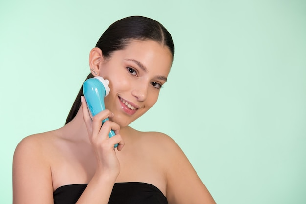 Concept of skin care, healthy firm skin. Young woman holding face massager on her face.