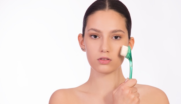 Concept of skin care, healthy smooth skin, peeling, facial treatment. Young woman holding a face brush on her face.