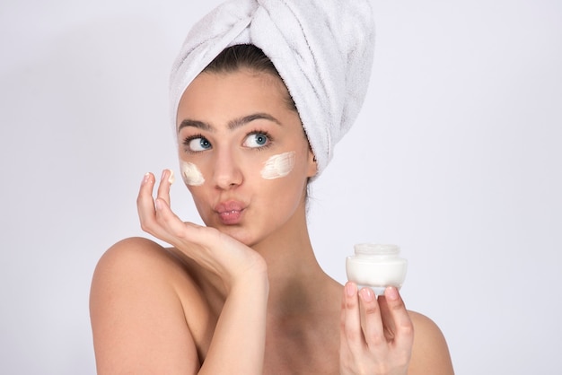 Concept of skin care and skin products, cremes and moisturizers. Girl model with face cream under her eyes and towel around her head.