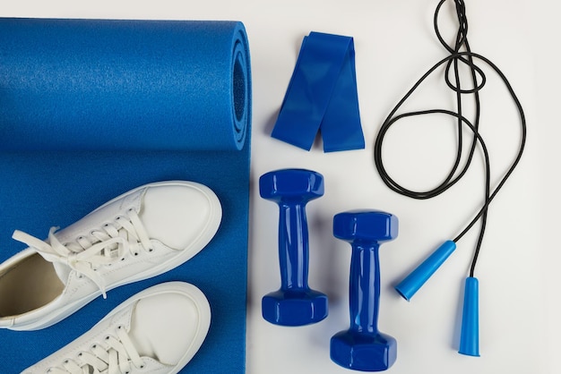 The concept of sports accessories Photo of white sneakers blue dumbbells and a blue exercise mat and other sports equipment
