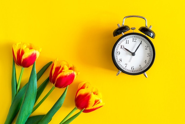 Concept of spring time. Red tulips on yellow background near the clock. Fresh flatlay