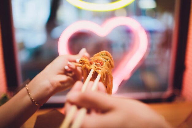 concept of street food chinese japanese noodles with chicken and vegetables in disposable paper utensils copy space selective focus on the background of a neon lamp in the shape of a heart