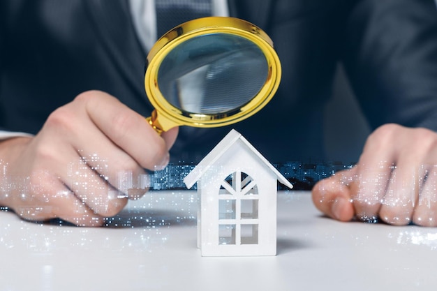 The concept of the study and inspection of the property Looking through a magnifying glass at a model home