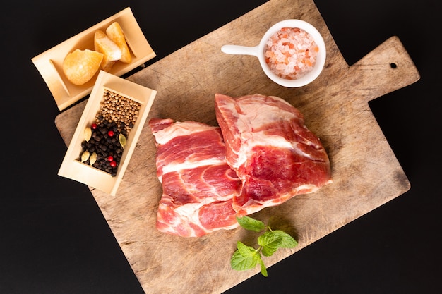 Concept stuk vlees zonder been Varkensvlees kraag op snijplank met specerijen op zwarte achtergrond met kopie ruimte