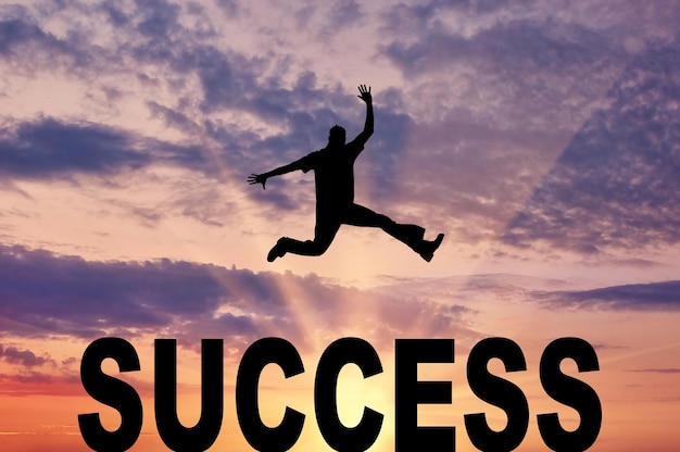 Концепция успеха. Человек прыгает через слово успех на фоне вечернего неба