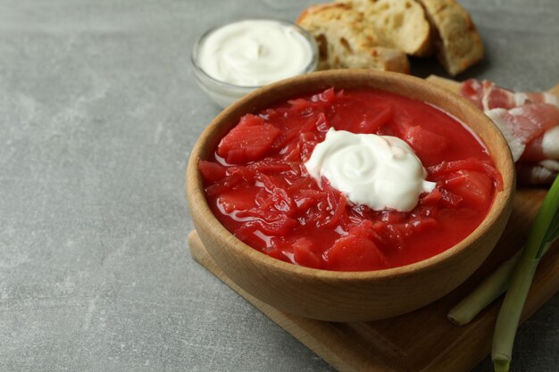 Concept of tasty eating with borscht and ingredients on gray table