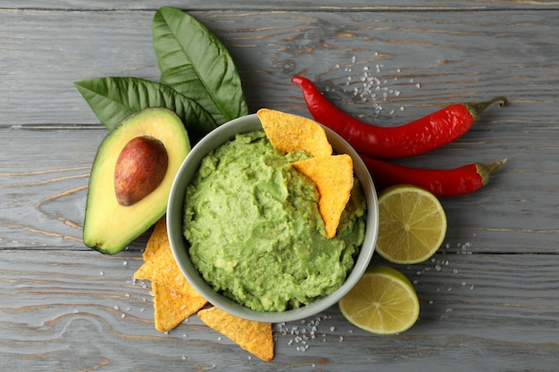 Concept of tasty eating with bowl of guacamole on wooden background, top view