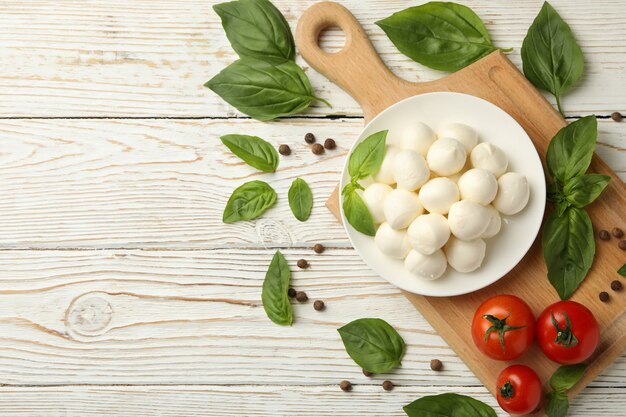 Concept of tasty eating with bowl of mozzarella cheese on white wooden background