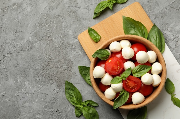 Concept of tasty eating with bowl of mozzarella, tomato and basil on gray table