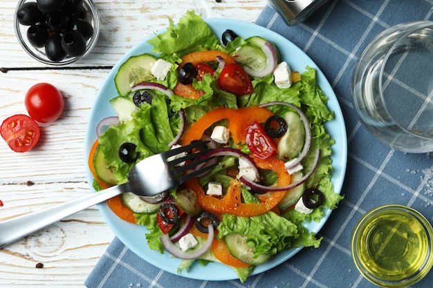 Photo concept of tasty eating with greek salad on white wooden table