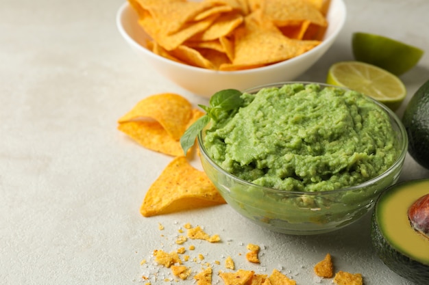 Concept of tasty eating with guacamole and chips on white textured background, space for text