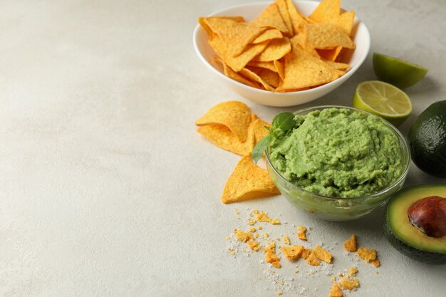 Concept of tasty eating with guacamole and chips on white textured background, space for text