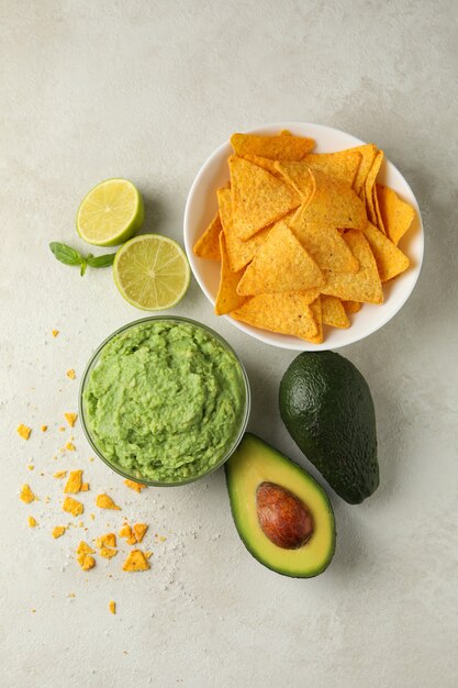 Concept of tasty eating with guacamole and chips on white textured background, top view