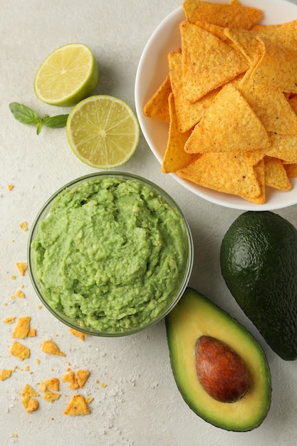 Concept of tasty eating with guacamole and chips on white textured background, top view