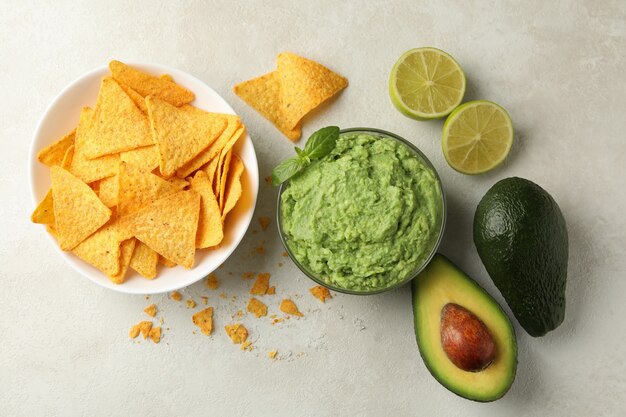 Concept of tasty eating with guacamole and chips on white textured background, top view