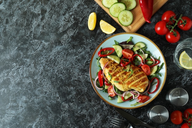 Concept of tasty eating with salad with grilled chicken on black textured table