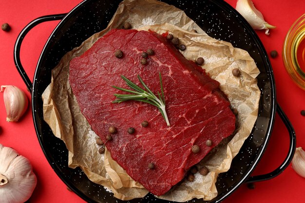 Concept of tasty food with raw beef steak on red background