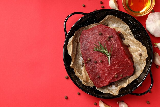 Concept of tasty food with raw beef steak on red background