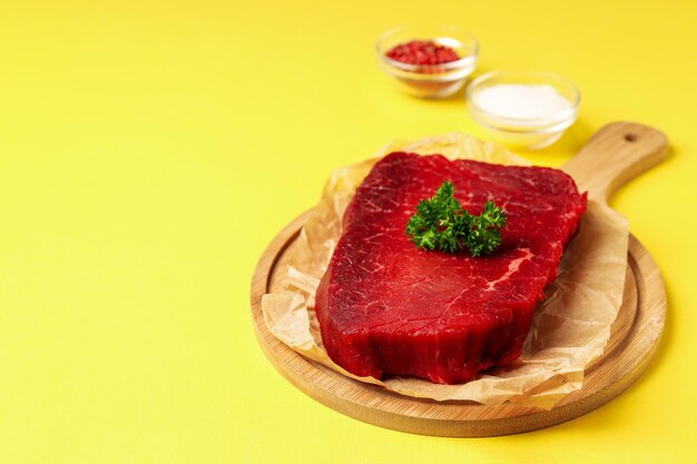 Concept of tasty food with with raw beef steak on yellow background