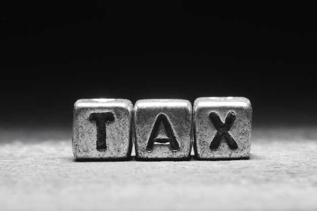 Concept of tax. The inscription on metal 3D cubes isolated on a black background, grunge style