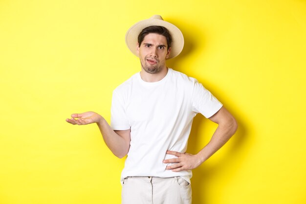 Concept of tourism and summer. Young skeptical tourist complaining, looking judgemental, standing over yellow background