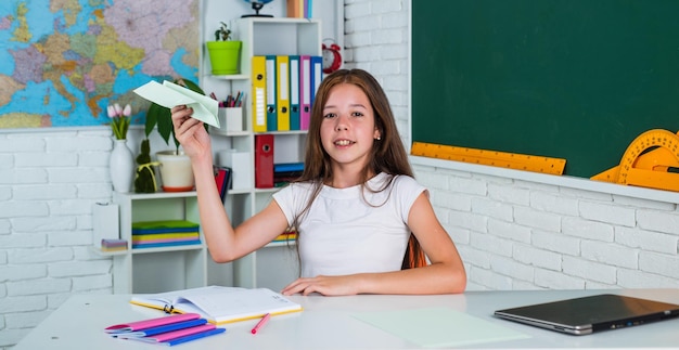 Concept of travel child pupil sit at table girl is college student back to school teen girl work in classroom near blackboard cheerful kid learning subject modern education knowledge day