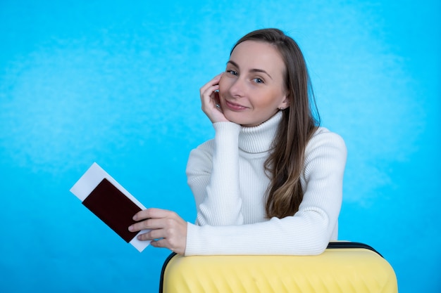 Concept of travel. happy woman with suitcase and passport on blue wall.