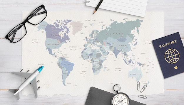 Concept of travel organization Airplane model passport compass glasses pad and pencil on world map Copy space in the middle Top view flat lay