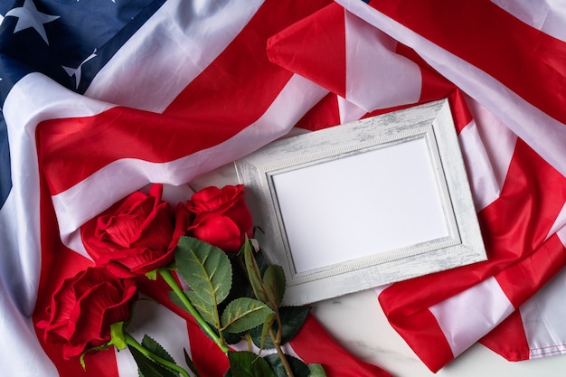 미국 독립 기념일 또는 현충일의 개념. 국기와 붉은 장미는 액자가 있는 밝은 대리석 테이블 배경 위에 있습니다.
