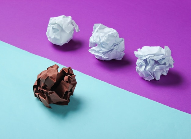 The concept of uniqueness, racial discrimination. White and brown crumpled paper balls on purple blue table. Minimalism business