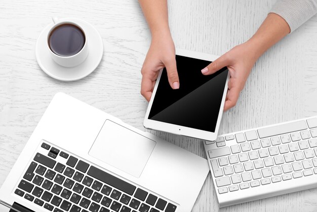 Concept of using electronics. Businesswoman works at office, close up. Computer, laptop, tablet, cup of coffee and other things on the table. Top view