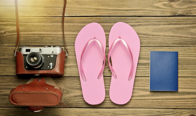 Il concetto di vacanza sulla spiaggia, turismo. priorità bassa del viaggiatore di estate. infradito, retro macchina fotografica, passaporto su fondo di legno. vista dall'alto. lay piatto