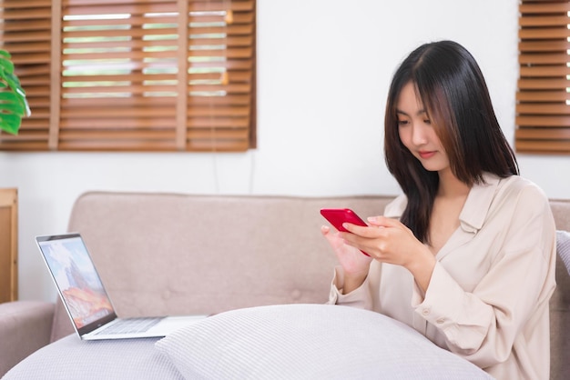Concept van activiteit in de woonkamer Aziatische vrouw gebruikt smartphone om op sociale media op de bank te surfen