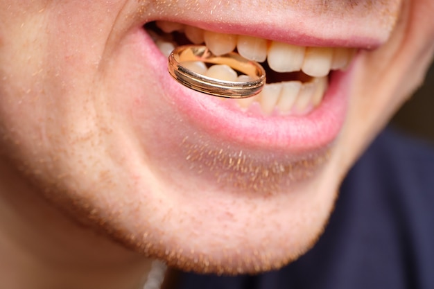 Concept van de ondergeplukte mens die een trouwring in zijn tanden houdt.