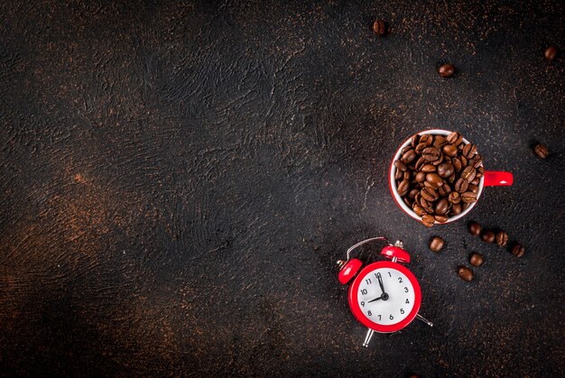 Concept van een vrolijke, goede start van de dag, ochtendkoffie. Donkere roestige achtergrond met koffiebonen, een wekker en een kopje koffie. Bovenaanzicht kopie ruimte