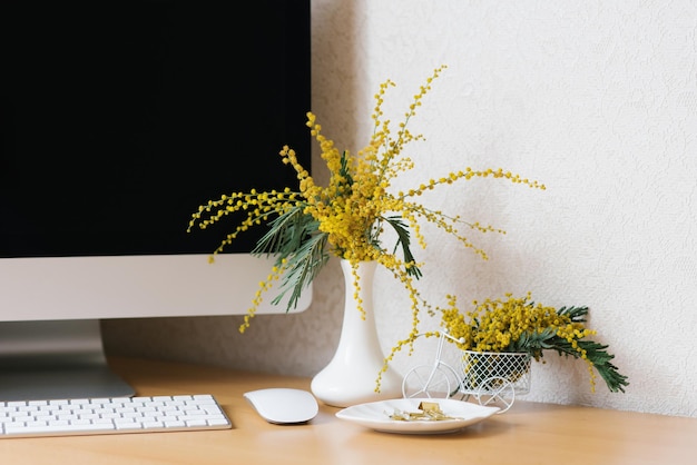 Concept van een zakelijke freelancer blogger de laptop staat op een houten tafel tegen een witte muur met een mimosa in een vaas