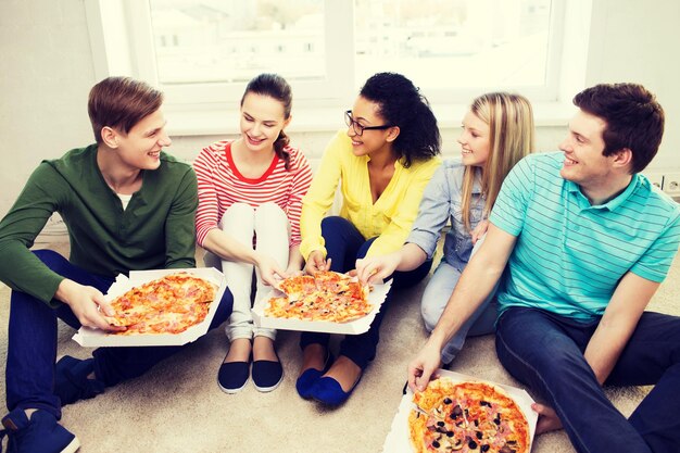 concept van eten, vrije tijd en geluk - vijf lachende tieners die thuis pizza eten