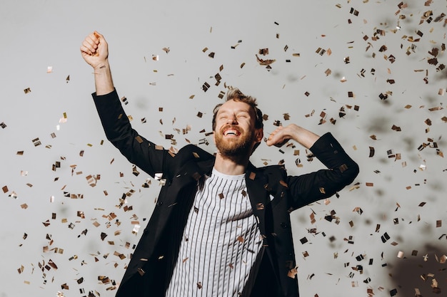 Concept van feest en overwinning Stijlvolle jonge man geïsoleerd op een witte achtergrond onder glinsterende confetti