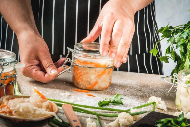 Concept van gefermenteerde maaltijd. Thuis ingeblikt voedsel en knuppels. Veganistisch eten. Groenten. De vrouwen kokende zuurkool van de persoon. Blikken met behoud, broccoli, wortelen, greens, uien.