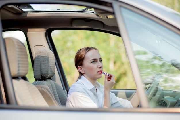 Concept van gevaar rijden. Jonge vrouw bestuurder roodharige tiener meisje schilderij haar lippen doen toepassing make-up tijdens het besturen van de auto