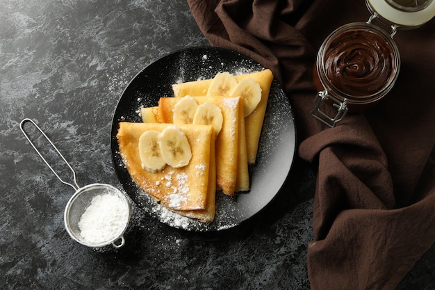 Concept van heerlijk ontbijt met pannenkoeken met suikerpoeder en banaan op zwarte smokey achtergrond