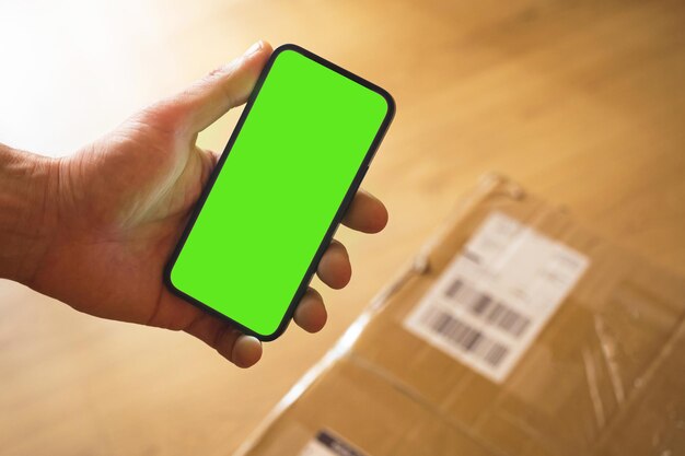 Concept van het ontvangen van groot pakket thuis, smartphone mockup groen scherm met plaats voor uw tekst voor reclame, man houdt mobiele telefoon vast terwijl bezorgservice pakketdoos naar huisdeur verzendt